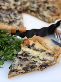 a slice of mushroom and cheese quiche on a white plate with a knife and fork