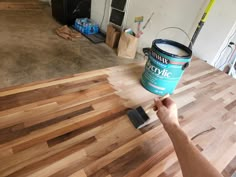 a person holding a paint can on top of a hard wood floor in a room