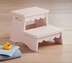 a pink wooden step stool with a rubber ducky toy on the floor next to it