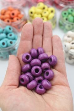 a hand is holding some beads in front of many other colors and sizes on the table