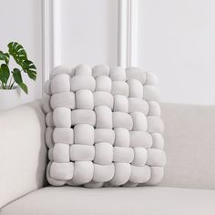 a white pillow sitting on top of a couch next to a plant