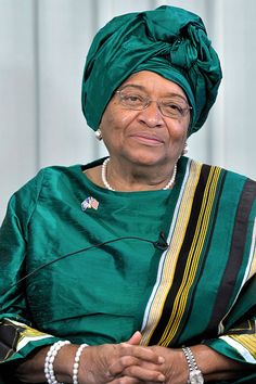 an older woman wearing a green head scarf and glasses sitting in front of a building