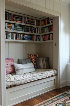 there is a white bench with bookshelves in the corner and pillows on it