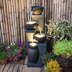 an outdoor fountain with three lit candles in it and potted plants next to it