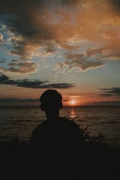 the silhouette of a person standing in front of an ocean at sunset with clouds above them