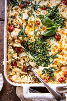 a casserole dish with spinach, cheese and tomatoes in it on a wooden table