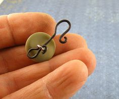 a hand holding a small metal hook with a button on it's back end