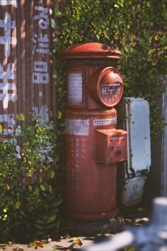 an old red fire hydrant sitting in front of a wall with writing on it