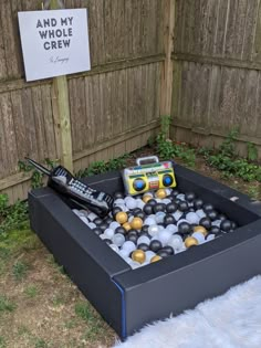 a box filled with balls and remotes on top of a grass covered yard next to a fence