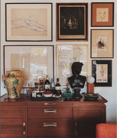 there are many framed pictures on the wall next to a dresser with bottles and vases