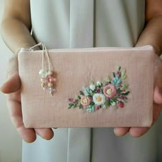 a woman is holding a pink purse with flowers on the front and side, in her hands