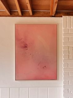 a painting hanging on the wall in a room with white brick walls and wood beams