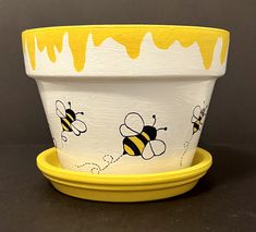 a yellow and white flower pot with bees painted on the side, sitting on a black surface