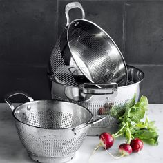 several stainless steel pots and pans with radishes next to them on a marble countertop