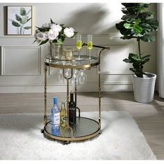 a bar cart with wine glasses and bottles on it in front of a potted plant