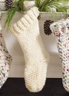 three knitted stockings hanging from a mantle with pine cones and needles on them,