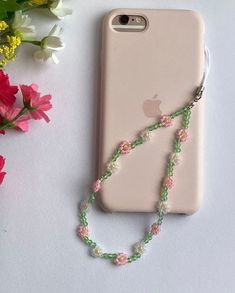 an iphone case with a beaded necklace attached to it next to flowers and a cell phone