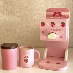 a pink coffee maker and cup with strawberries on the side, next to it