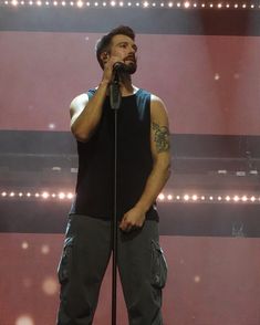 a man standing on top of a stage holding a microphone in his hand and wearing cargo pants