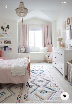 a white bedroom with pink curtains and pillows on the window sill next to a bed