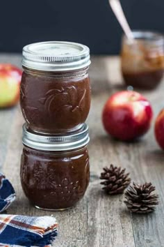 three jars filled with chocolate pudding sitting on top of a wooden table next to apples