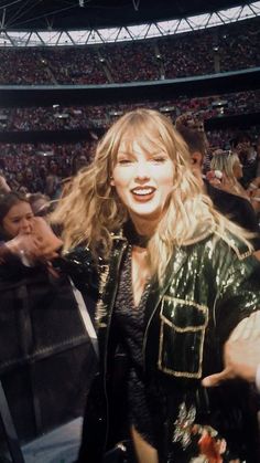 taylor swift at a concert with fans in the stands and one hand on her hip