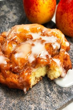 an apple cinnamon roll with icing sitting on top of a counter next to two apples