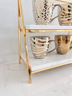 gold and white coffee cups are stacked on a marble serving tray in front of a white wall