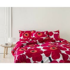 a bed with red flowers on it in a white room next to a table and chair