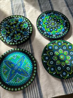 four decorative plates sitting on top of a striped tablecloth covered table with blue and green designs