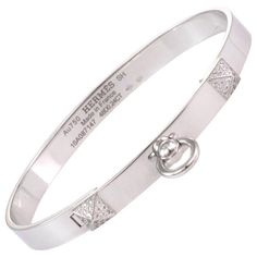 This stunning Collier de Chein collection is by Hermes, it features an authentic bangle crafted from 18k white gold with a high polished finish featuring a 6mm wide band. The front of the bangle has two small pyramid like design set with diamond and the center has a door knocker ring dangling below. It is signed by the designer with the serial number, gold content and diamond weight. Brand: Hermes Hallmark: Au750 Hermes SH Made in France 16A087147 48D0.24ct Diamond: 0.24ct (48 diamonds) Material Luxury Silver Platinum Bracelets, Luxury Platinum Bangle Bracelet, Designer White Gold Round Bracelets, Designer White Gold Bracelets, Luxury Hallmarked Platinum Bracelets, Luxury Polished Platinum Bracelets, Luxury Platinum Hallmarked Bracelets, Luxury Platinum Bracelets With Polished Finish, Luxury Polished Platinum Bracelet