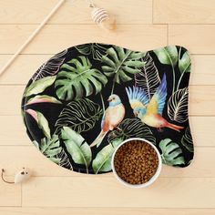 a dog bowl mat with two birds and tropical leaves on it next to a cat food dish