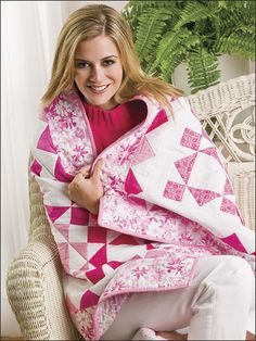 a woman sitting on a chair holding a pink and white quilt