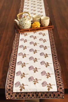 a table runner with teapots and cups on it in front of a wooden table