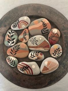 some rocks are sitting in a bowl with leaves and flowers painted on them, along with other stones