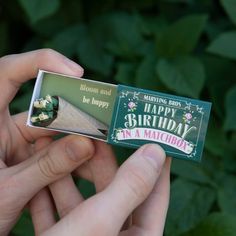 someone is holding a matchbox with a happy birthday message on it in front of some plants