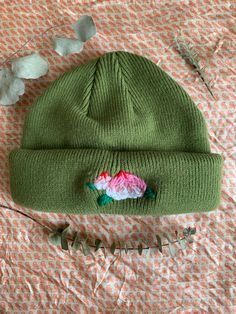 a green knitted hat with pink and blue flowers on it sitting on a bed