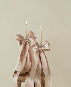 two candles with pink bows on them sitting in front of a white wall and wooden chair