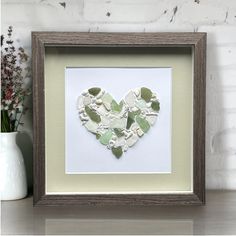 a heart shaped piece of paper in a frame on a table next to some flowers