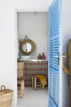 an open door leading to a dining room with blue shutters and wicker chairs