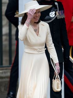 the queen of england is wearing a white hat and dress while she walks with her hand on her head