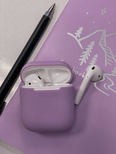 an apple airpods sitting on top of a purple book next to a black pen