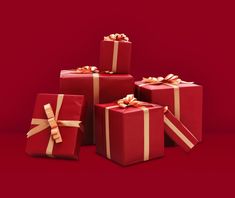 five red wrapped presents with gold ribbons and bows on them, all stacked up together