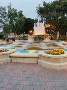 the fountain is surrounded by flowers and trees