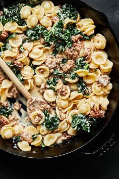 a skillet filled with pasta, meat and spinach