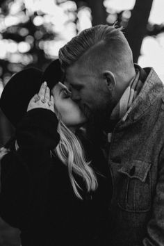 a man and woman kissing each other in black and white with trees in the background