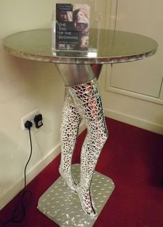 a metal table with a book on it and a pair of legs in the shape of a woman