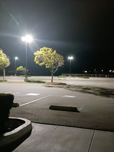 an empty parking lot at night with street lights shining on the trees and bushes in the foreground