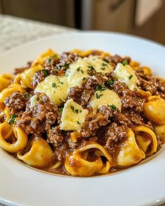 a white plate topped with pasta covered in meat and cheese on top of a table