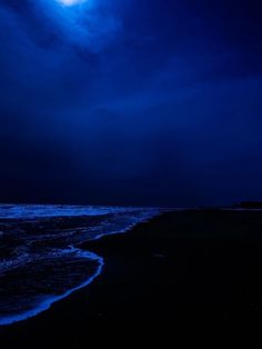 a full moon is shining over the ocean on a dark night with waves coming in